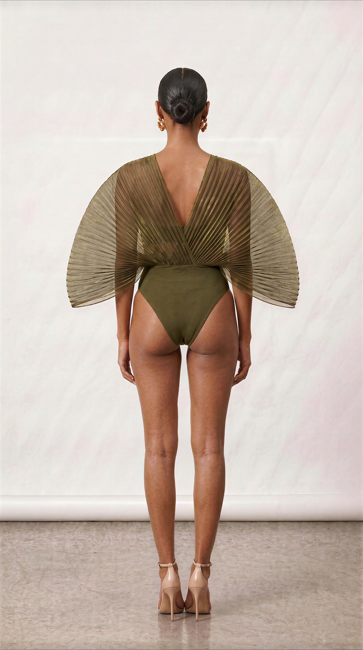 [INPUTS: PRESERVE THREE-QUARTER COMPOSITION FROM The New Black (51).jpg | RECOLOR OUTFIT TO OLIVE GREEN FROM The New Black (60).jpg | SWAP HEAD, PROFILE & SKIN TONE 100% TO Model_Reference_2.jpg]

Model Profile (MODEL REFERENCE 2 LOCK):

Model Reference 2 from Model_Reference_2.jpg positioned in a dynamic three-quarter angle pose (torso angled at 45 degrees, turned slightly left while facing into the studio).

Lock onto her exact facial features, warm-bronze skin tone, and natural matte skin texture.

Hair 