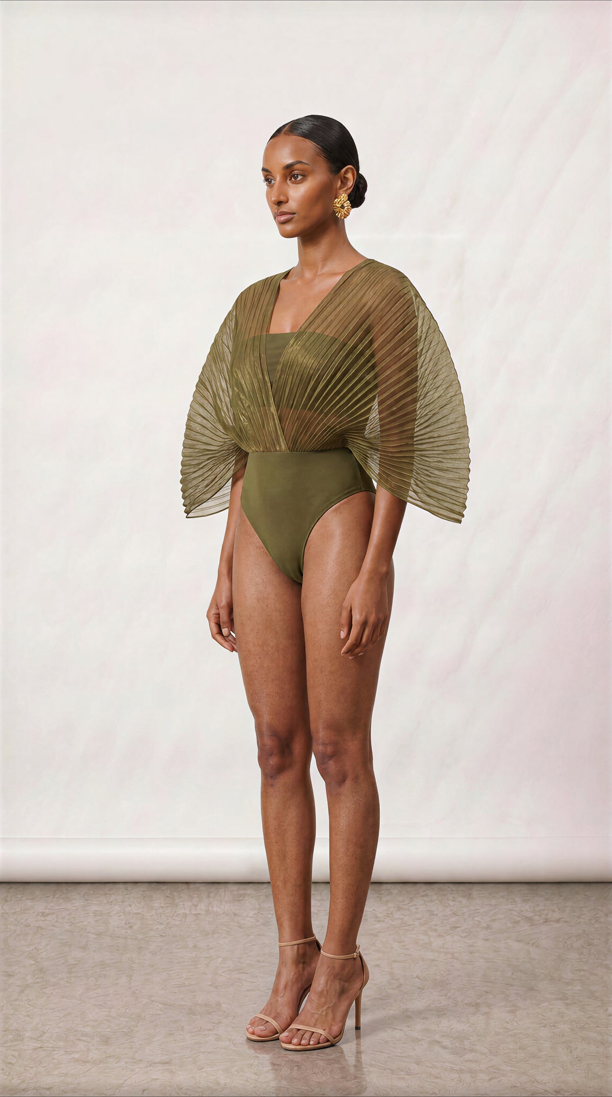 [INPUTS: PRESERVE THREE-QUARTER COMPOSITION FROM The New Black (51).jpg | RECOLOR OUTFIT TO OLIVE GREEN FROM The New Black (60).jpg | SWAP HEAD, PROFILE & SKIN TONE 100% TO Model_Reference_2.jpg]

Model Profile (MODEL REFERENCE 2 LOCK):

Model Reference 2 from Model_Reference_2.jpg positioned in a dynamic three-quarter angle pose (torso angled at 45 degrees, turned slightly left while facing into the studio).

Lock onto her exact facial features, warm-bronze skin tone, and natural matte skin texture.

Hair 